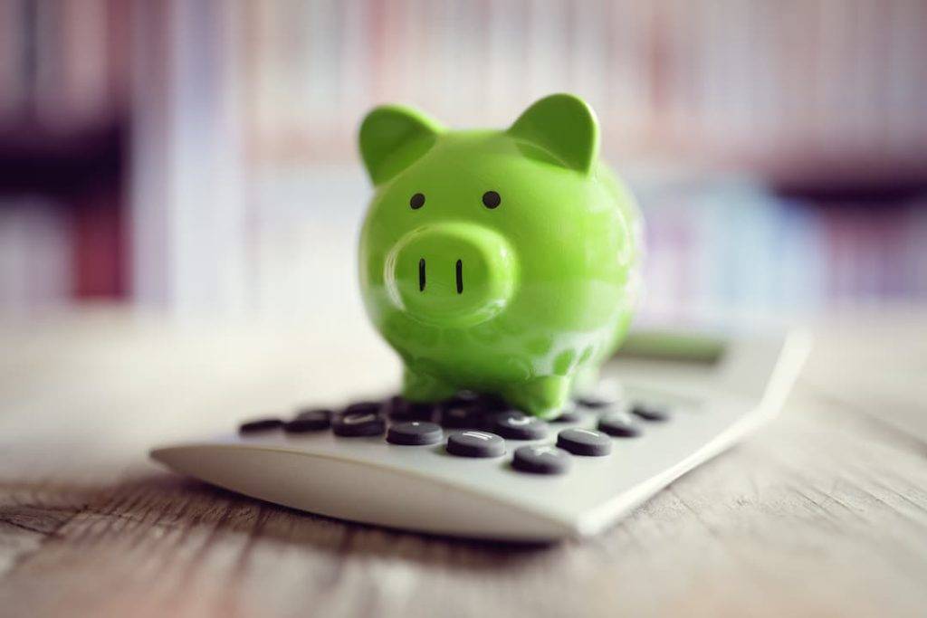 Saving Costs - Green Piggy Bank On A Calculator